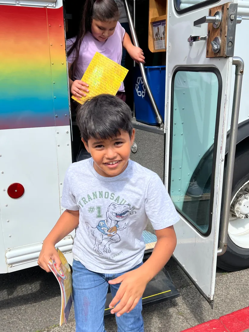 A smiling boy steps off the Bookmobile holding a book