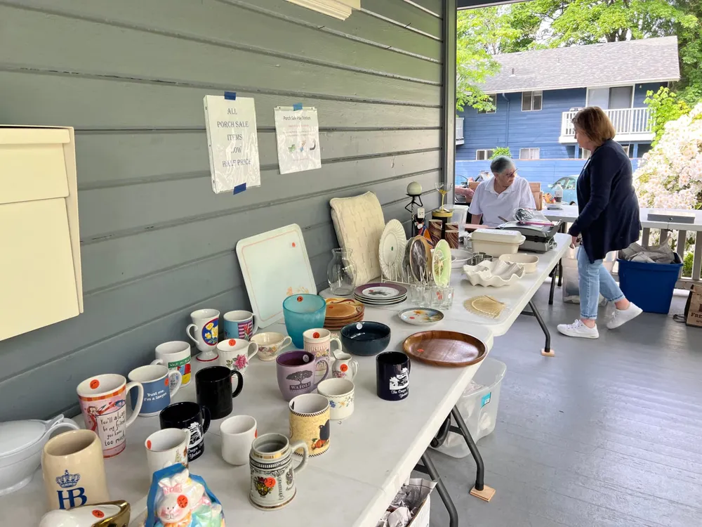 Tables of mugs, dishes, and housewares on the Daue House porch during the Porch Sale